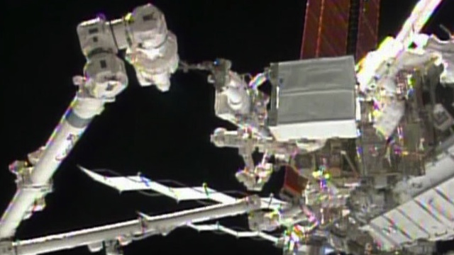 PRE-CHRISTMAS SPACEWALK. Astronaut Rick Mastracchio holds the degraded pump module while the International Space Station's robotic arm guides the module to a grapple fixture. Image courtesy NASA TV