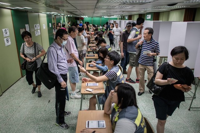 VOTING FOR DEMOCRACY. A volunteer (C) hands a voter's ID card at a polling station in Hong Kong on June 22, 2014. Philippe Lopez/AFP