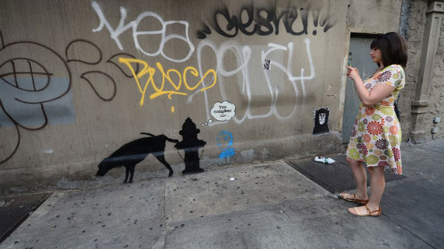ART OR NOT? A woman takes a picture of a street art graffiti by elusive British artist Banksy in New York. AFP Photo 