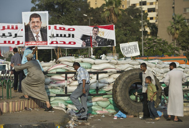 DEFUSING A CRISIS. Egyptian supporters of deposed president Mohamed Morsi (portrait) walk past a barrier of sandbags to join a rally organized by the Muslim Brotherhood group in his support outside Rabaa al-Adawiya mosque in Cairo on August 4, 2013. An Egyptian court set a trial date for Muslim Brotherhood leaders in a move likely to enrage supporters of the ousted Islamist president. TOPSHOTS/AFP PHOTO/KHALED DESOUKI