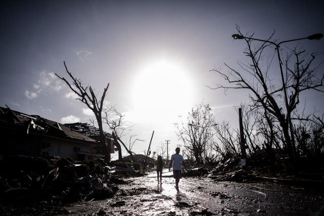 LOSSES. A man and a woman walk past broken trees as the sun rises on the 7th day of the Typhoon Haiyan disaster in Tacloban, Leyte on November 15, 2013. AFP PHOTO/Philippe Lopez