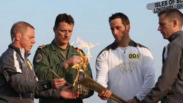 UNITED KINGDOM, LANDS END: British sailor Ben Ainslie (2R), the first torchbearer lights the Olympic torch from the Olympic flame at Land's End, the southwesterly tip of England on May 19, 2012 as he begins the first leg of the torch relay around Britain and Ireland. AFP.