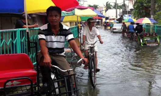 ADAPTING TO FLOOD. Joey Dionido drives a pedal tricycle that was built to brave floodwaters. Photo by Voltaire Tupaz