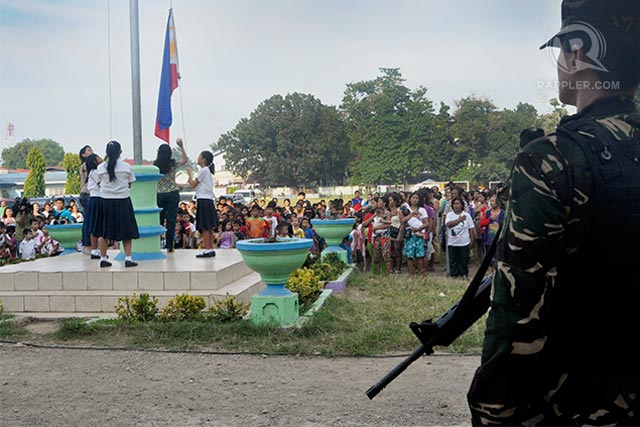 FLAG-RAISING. A soldier looks over a group of students and teachers raising the Philippine flag during the reopening of classes in Sta. Maria Central School. Photo by LeAnne Jazul/Rappler 