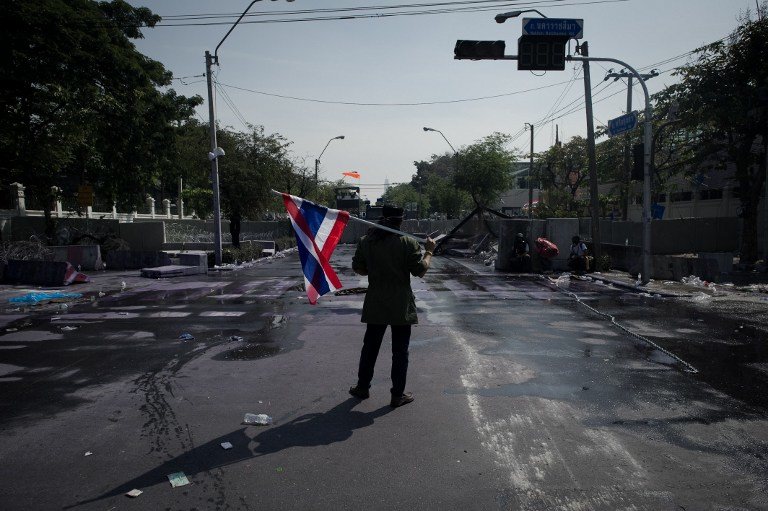 DEFIANCE. An anti-government protester stand alone with a national flag infront of a riot police barricade outside the police headquarters during an ongoing rally in Bangkok on December 2, 2013. AFP/ Nicolas Asfouri