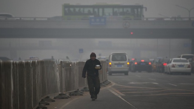 SHROUDED IN SMOG. A man carries food as he walks between traffic during heavily polluted weather in Beijing in this file photo dated January 29, 2013. AFP PHOTO / Ed Jones