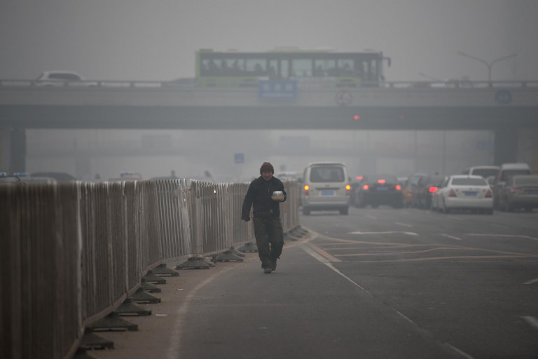 SHROUDED IN SMOG. A man carries food as he walks between traffic during heavily polluted weather in Beijing on January 29, 2013. AFP PHOTO / Ed Jones