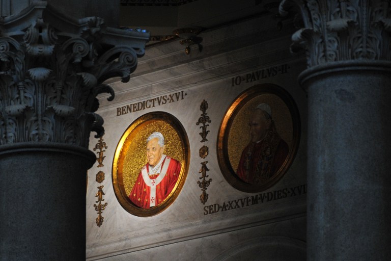 The portrait of Pope Benedict XVI (L) is displayed next to Pope John Paul II's on a wall of the St Paul Outside the Walls’ basilica on February 13, 2013 in Rome. The portraits of each pope are displayed in a frieze extending above the columns separating the four aisles and naves. AFP PHOTO / TIZIANA FABI
