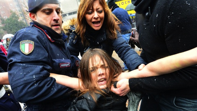 'BASTA BERLUSCONI' A topless feminist is arrested by riot policemen outside the polling xtation where former Prime Minister Silvio Berlusconi casted his ballot on February 24, 2013 in Milan. AFP PHOTO / GIUSEPPE CACACE