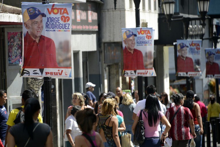 CAMPAIGN IN CARACAS. People walk by campaign posters for the upcoming municipal elections from SucreTown candidate for the Socialist Party, Jorge Rodriguez in Caracas, on December 6, 2013 in Caracas. AFP / Leo Ramirez