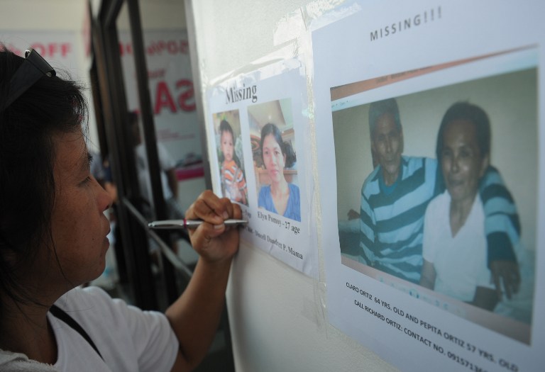 DESPERATE SEARCH. A relative of one of the missing passengers writes down contact numbers on pictures of missing kin displayed at the office of the ferry involved in a collision, in Cebu City, August 18, 2013. Photo by AFP/Ted Aljibe
