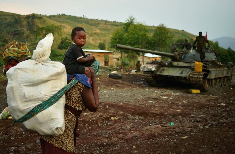 CONFLICT ZONE. A woman carrying a child on her shoulders walks past a Military of the Democratic Republic of Congo (FARDC) tank in Goma on August 31, 2013. AFP /Carl de Souza