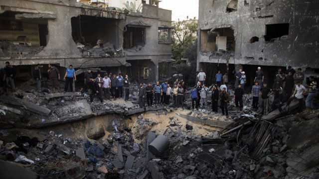 AFTERMATH. Palestinian men gather around a crater caused by an Israeli air strike on the al-Dallu family's home in Gaza City on November 18, 2012. AFP PHOTO/MARCO LONGARI