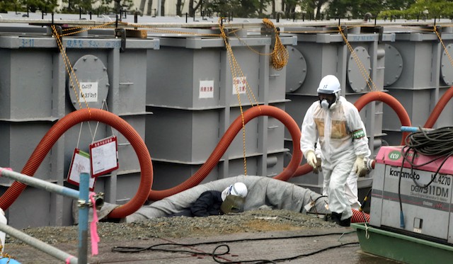TREADING CAREFULLY. A Tokyo Electric Power Company (TEPCO) employee in protective clothing works around water tanks at the Fukushima nuclear power plant in Fukushima, Japan, 12 June 2013. Photo by EPA/Noboru Hashimoto / Pool
