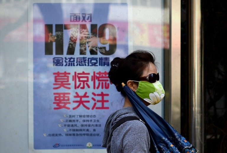 QUARANTINE. A woman wears a face mask as she walks past a poster showing how to avoid the H7N9 avian influenza virus, by a road in Beijing. The virus has since spread to at least one person in Hong Kong. Photo by AFP / Wang Zhao