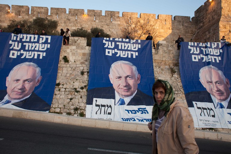 A woman walks in front of campaign posters of Israeli Prime Minister and Likud party leader Benjamin Netanyahu, with text reading in Hebrew: " Only Netanyahu will guard Jerusalem" along the walls of the old city of Jerusalem on January 20, 2013, ahead of the Israeli general election on January 22. AFP/ EMIL SALMAN