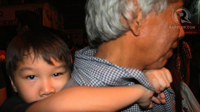 A CHILD IS CARRIED on the back of an elderly man, snaking through the crowd