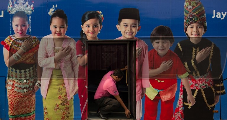 EQUAL OPPORTUNITY? Minorities in Malaysia are angered by new government policies favoring the native Malay majority, with experts saying it could make the country lose its best and brightest. In this photo, a man (C) opens a bus door through within a poster showing the Malaysia ethnic communities with traditional dress in Kuala Lumpur on September 25, 2013. AFP / Mohd Rasfan