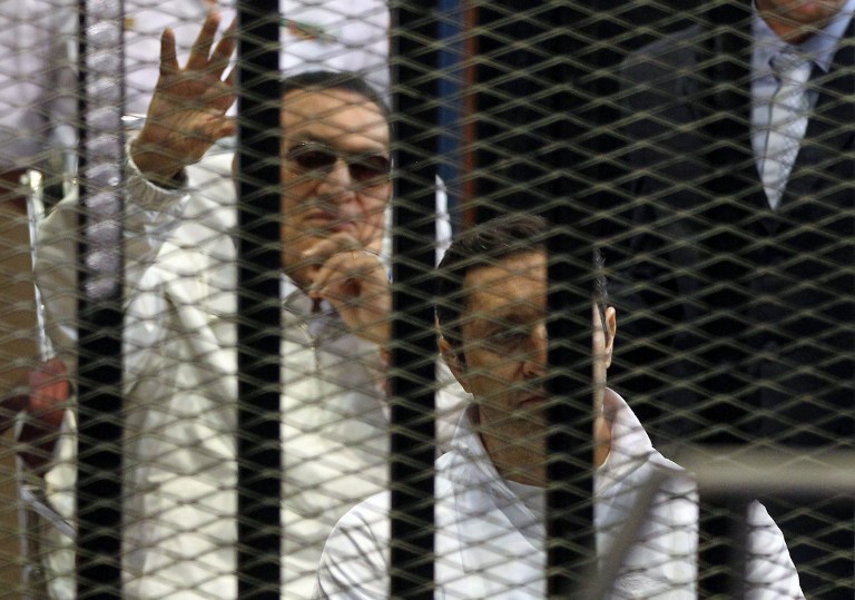 BEHIND BARS. Alaa Mubarak, son of ousted Egyptian president Hosni Mubarak, (back) sits in front of his father behind bars during a hearing in their retrial at the Police Academy in Cairo on April 13, 2013. AFP PHOTO / STR