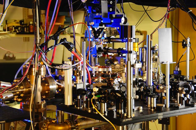 MOST ACCURATE. NIST's ultra-stable ytterbium lattice atomic clock. Ytterbium atoms are generated in an oven (large metal cylinder on the left) and sent to a vacuum chamber in the center of the photo to be manipulated and probed by lasers. Laser light is transported to the clock by five fibers (such as the yellow fiber in the lower center of the photo). Photo courtesy Burrus/NIST
