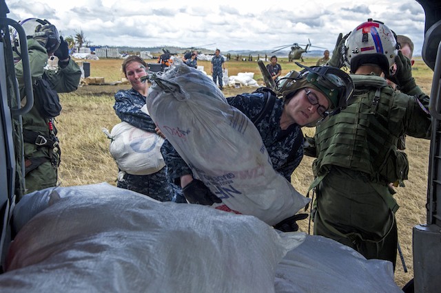 AID DELIVERY. U.S. Navy Petty Officer 3rd Class Deanna Coutts (C) loads a bag of supplies onto an MH-60S Seahawk helicopter to be airlifted to nearby villages in support of Operation Damayan in Tacloban, Philippines, Nov. 20, 2013. U.S. Navy photo by Petty Officer 2nd Class Trevor Welsh