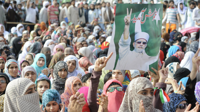 RETURN. Supporters holding a poster of Dr Tahir-ul-Qadri gather on a road as he is expected to arrive at in Islamabad, Pakistan in June 23, 2014. Dr Tahir-ul-Qadri was holed up inside an airplane in Lahore on 23 June after authorities denied it permission to land in the capital Islamabad, officials said. Photo by T. Mughal/EPA