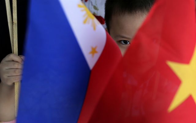 'ON SAME SIDE.' A Vietnamese child peers from Vietnam and Philippines flags while waiting for the arrival of Vietnam Prime Minister Nguyen Tan Dung at Villamor Airbase in Pasay, south of Manila, Philippines on May 21, 2014. File photo by Dennis Sabangan/EPA