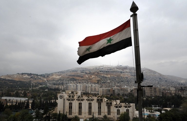 IN TATTERS. A Syrian flag flutters in the foreground with Damascus' Sheraton hotel (C) and Mount Qasyun in the backgound on December 12, 2013. Louai Beshara/AFP