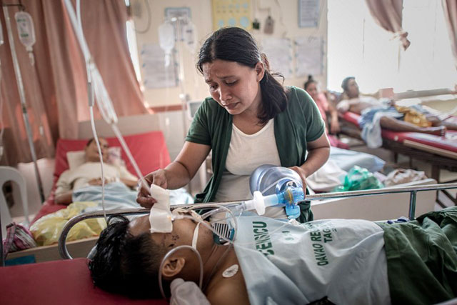 HUSBAND AND WIFE. A typhoon victim checks on her husband and pumps air into his lungs in a Tacloban hospital, after a leg amputation led to an infection. Photo by Philippe Lopez/AFP