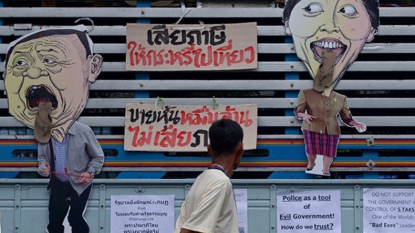  THAILAND, Bangkok : A Thai anti government protester (C) walks past protest placards as he attends a rally near Government House in Bangkok on December 16, 2013. The protests -- aimed at toppling Yingluck Shinawatra and curbing the influence of her older brother, ousted premier Thaksin Shinawatra -- have left five dead and more than 200 wounded in street violence, although tensions have abated in recent days. AFP PHOTO / PORNCHAI KITTIWONGSAKUL