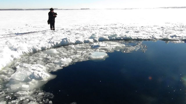 RUSSIAN FEDERATION, - : A handout photo taken on February 15, 2013, and provided by Chelyabinsk region police department shows a police officer standing near a six-metre (20-foot) hole in the ice of a frozen lake, reportedly the site of a meteor fall, outside the town of Chebakul in the Chelyabinsk region. Divers scoured today the bottom of a Russian lake for fragments of a meteorite that plunged to Earth in a blinding fireball whose shockwave injured 1,200 people and damaged thousands of homes. AFP PHOTO / CHELYABINSK REGION POLICE DEPARTMENT