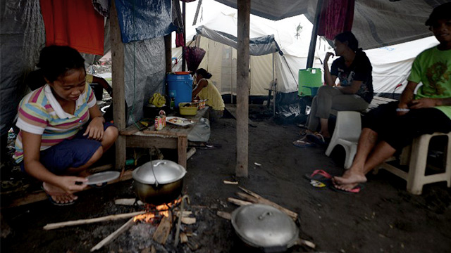 NO SHELTER. A Yolanda survivor prepares her family's meal in a tent serving as temporary shelter in Tacloban City. Photo by Ted Aljibe/ Agence France-Presse