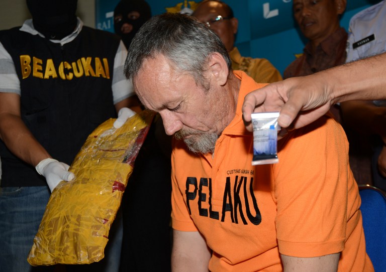 Antony Glen De Malmanche of New Zealand sits as evidence is placed next to him by customs security during a press conference at the customs office in Denpasar on Bali island on December 5, 2014. De Malmanche was arrested on December 1 carrying 1709 grams of methamphetamine in his bag at Bali International Airport. AFP PHOTO / SONNY TUMBELAKA